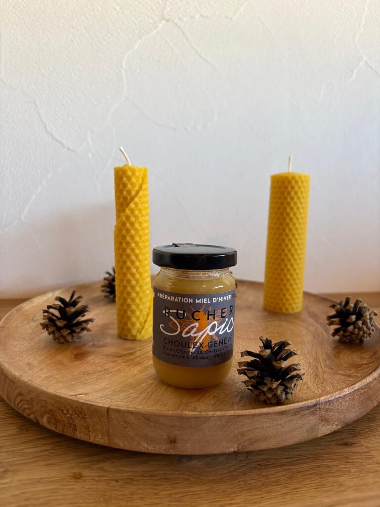 Pot de préparation miel d’hiver du Rucher SAPIC, entouré de bougies en cire d’abeille et de pommes de pin