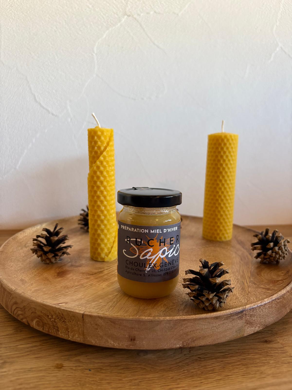 Pot de préparation miel d’hiver du Rucher SAPIC, entouré de bougies en cire d’abeille et de pommes de pin
