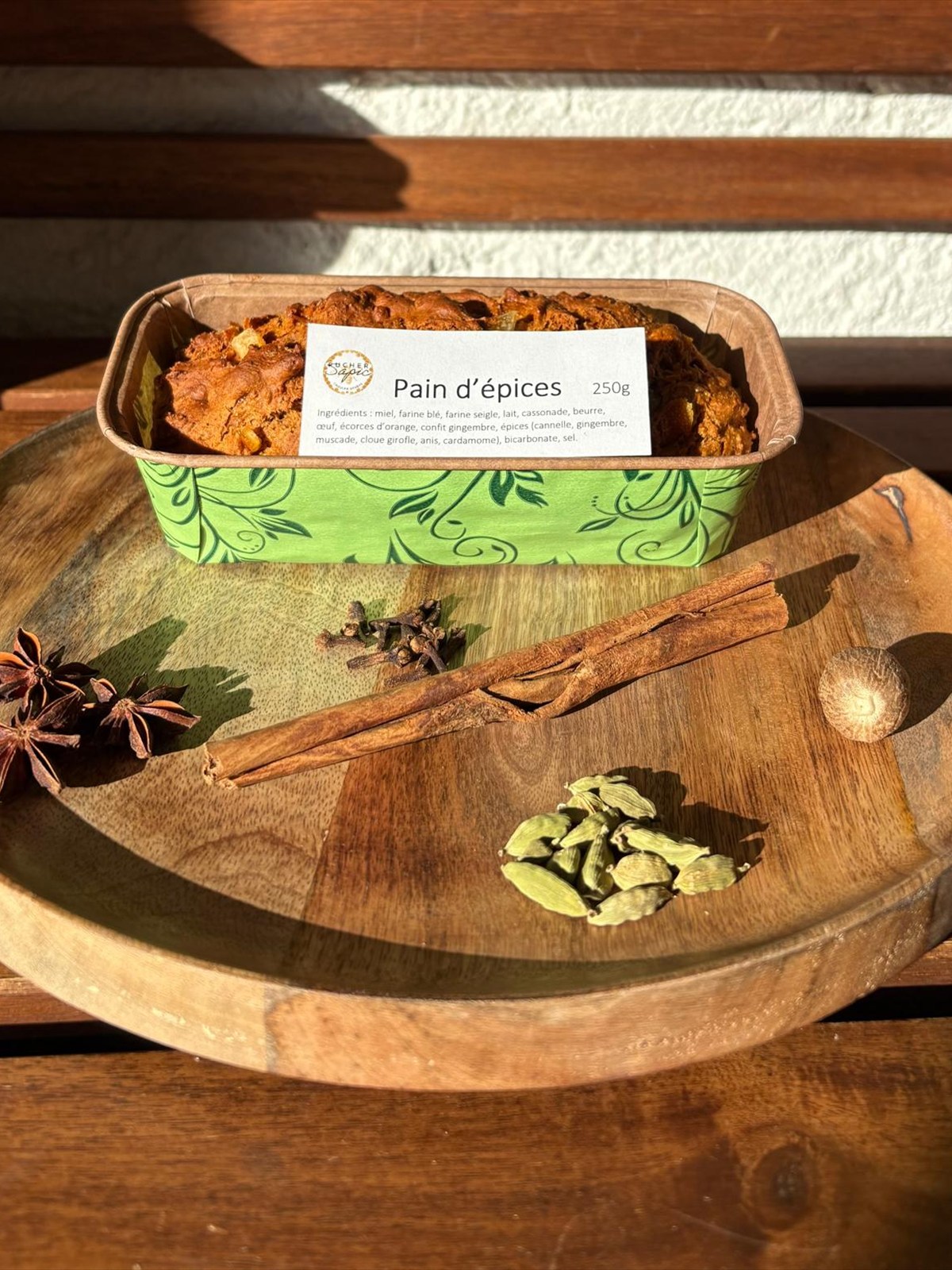 Pain d’épices du Rucher SAPIC, 250g, sur un plateau en bois avec badiane, cannelle, cardamome, clous de girofle et noix de muscade